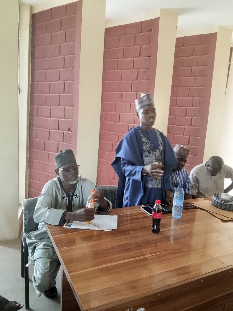 A community meeting with local leaders seated around a table.