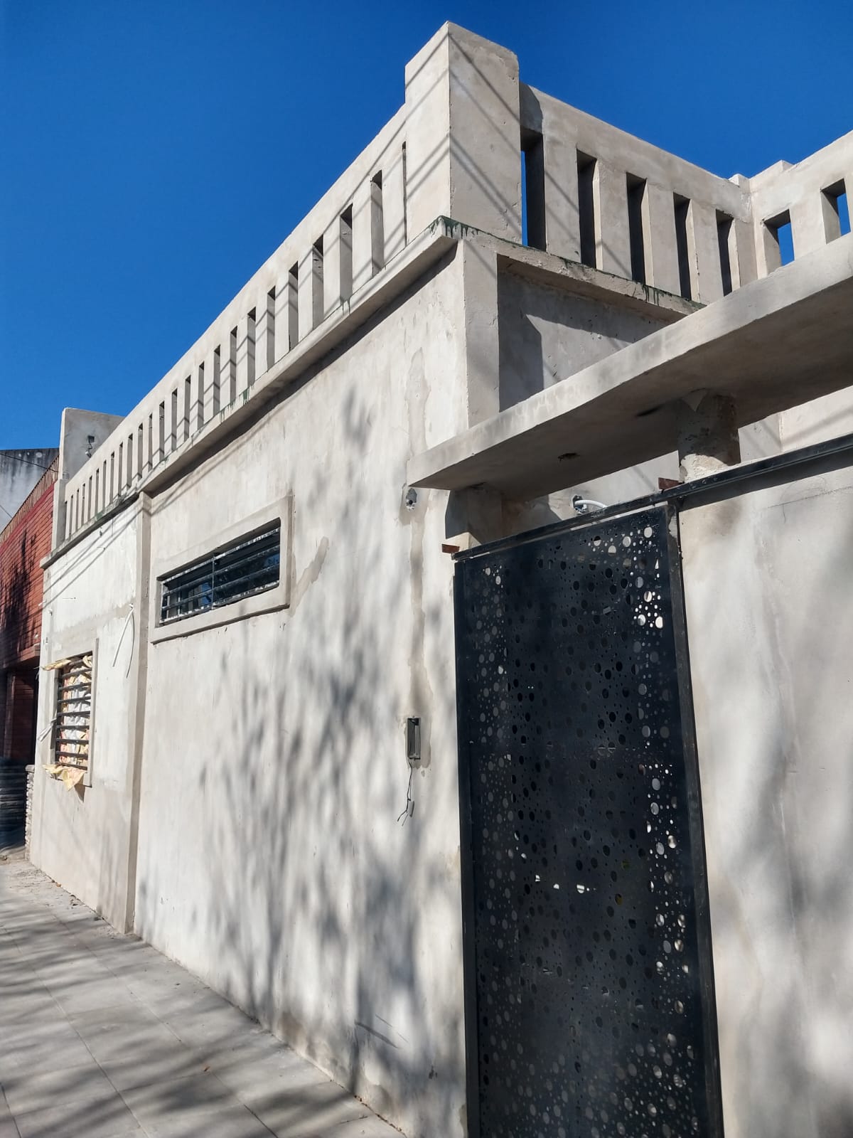 Fachada con puerta de chapa perforada decorativa, baranda de hormigon y revoque