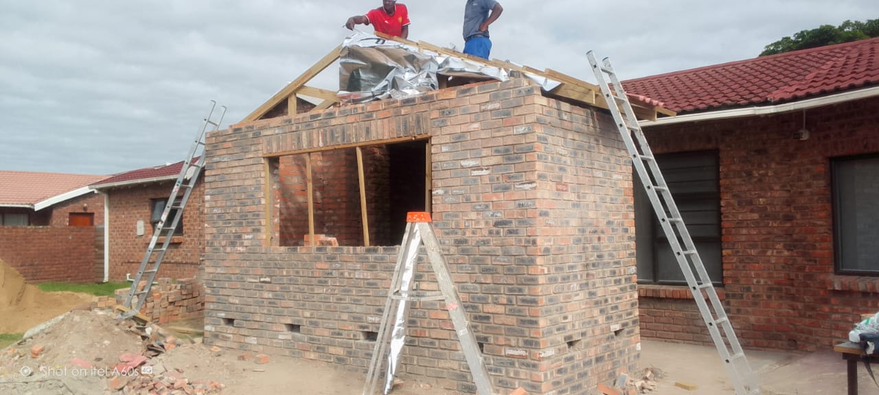 Before: Two workers on top of bare brick extension installing wooden roof trusses and foil sarking