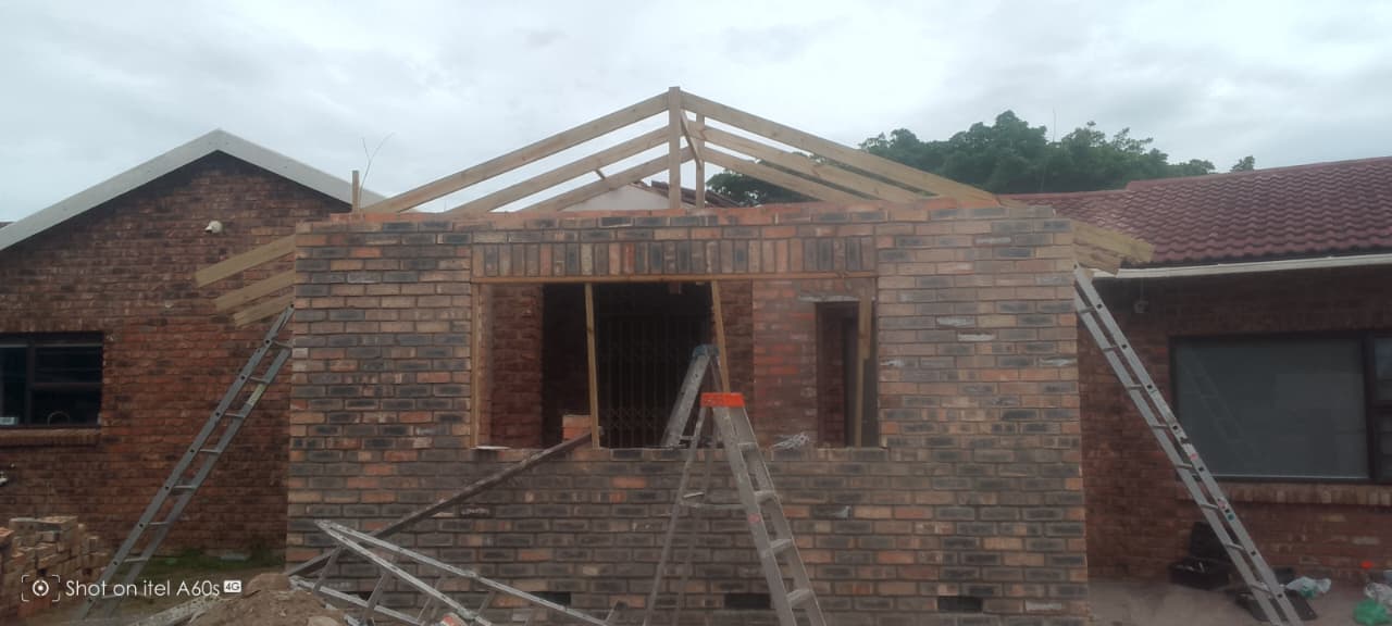 Front-on view of brick room with full A-frame wooden trusses erected, no tiles yet, grey sky