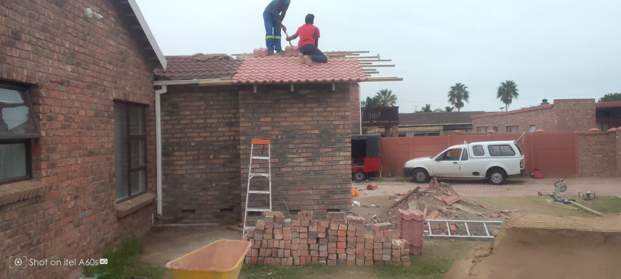 Two workers on completed red tile roof laying the final tiles, timber battens visible on right side