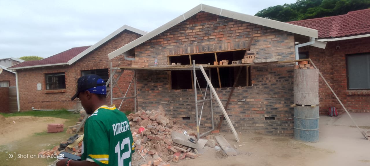 Wide scaffolding view of brick extension with partial fascia boards and second-storey level brickwork, overcast sky