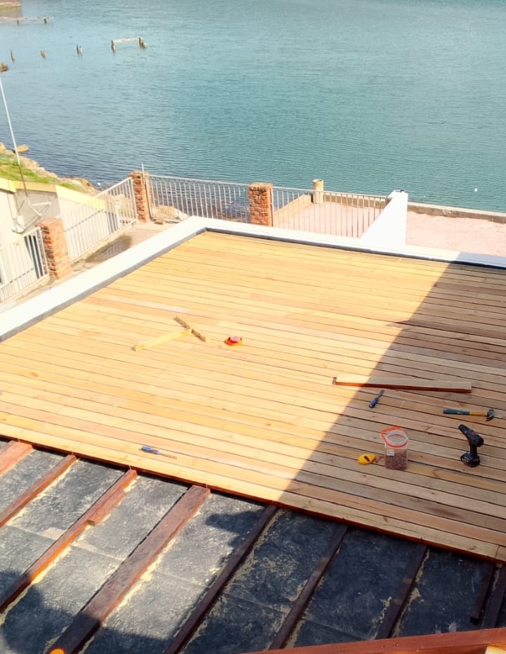 Before: Fresh natural pine deck boards freshly laid but unstained, tools scattered, lagoon view behind