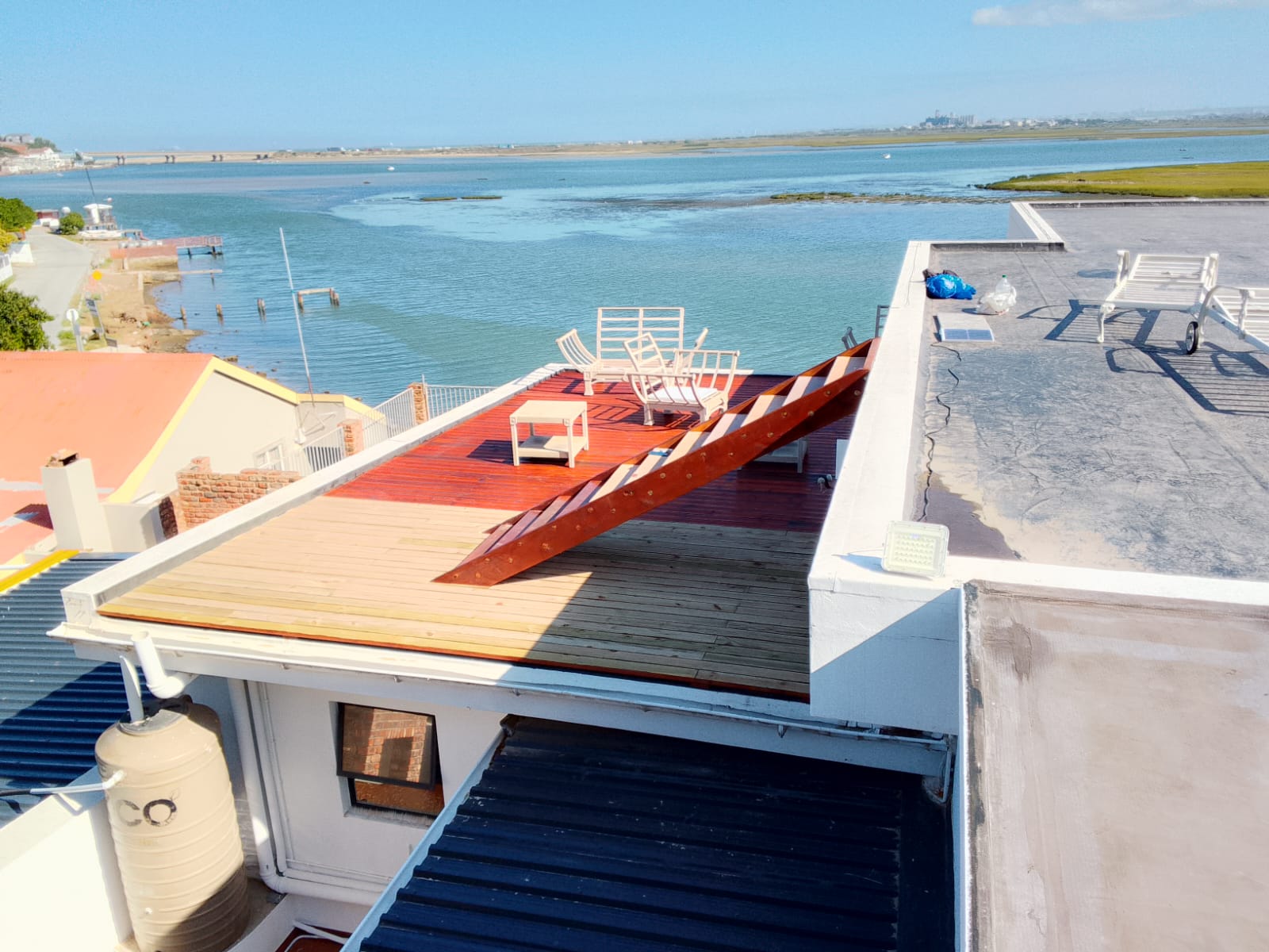 After: Completed rich mahogany-stained rooftop deck with chairs and tables, stunning open lagoon view