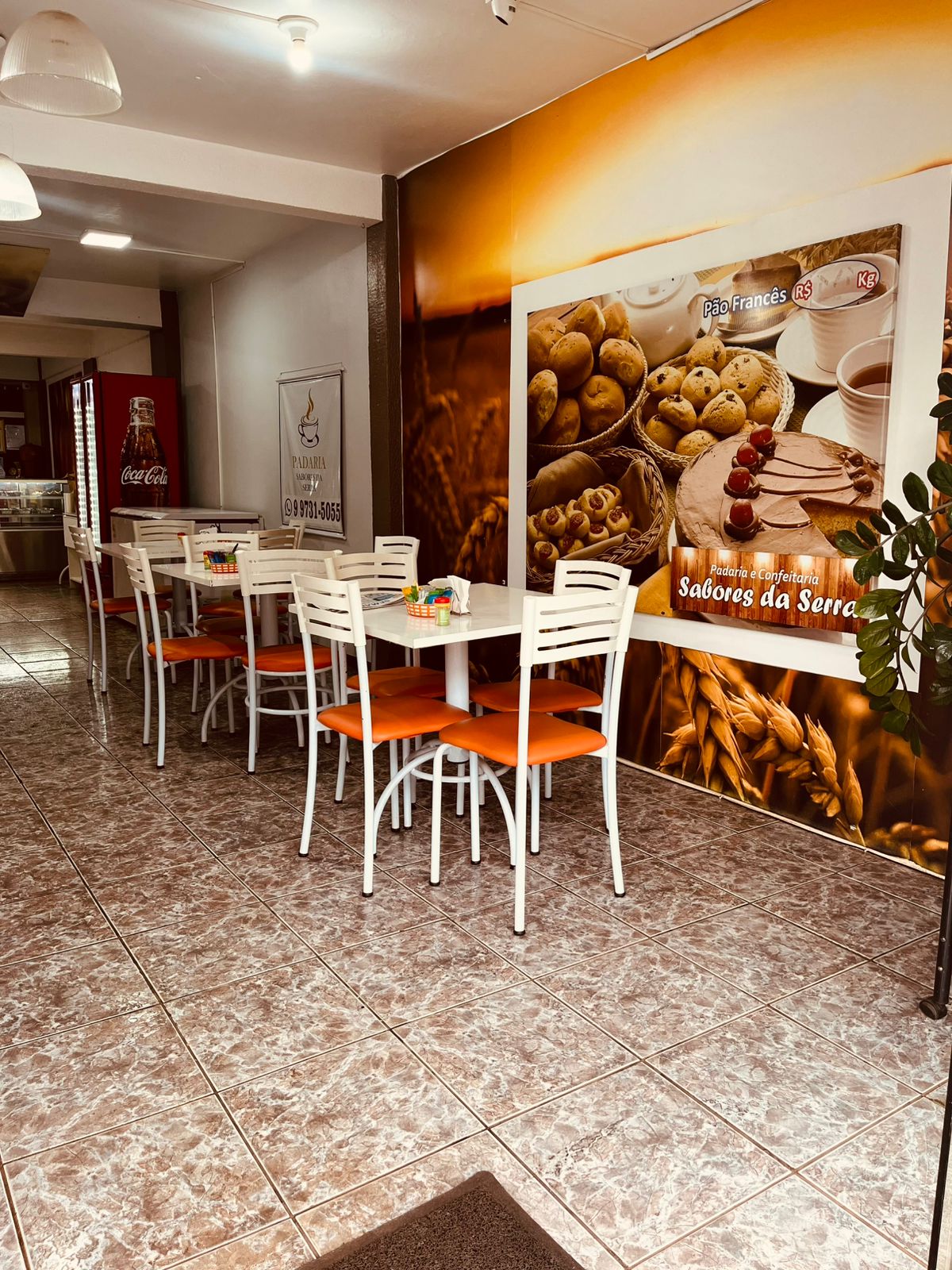 Salao com mesas e painel da padaria