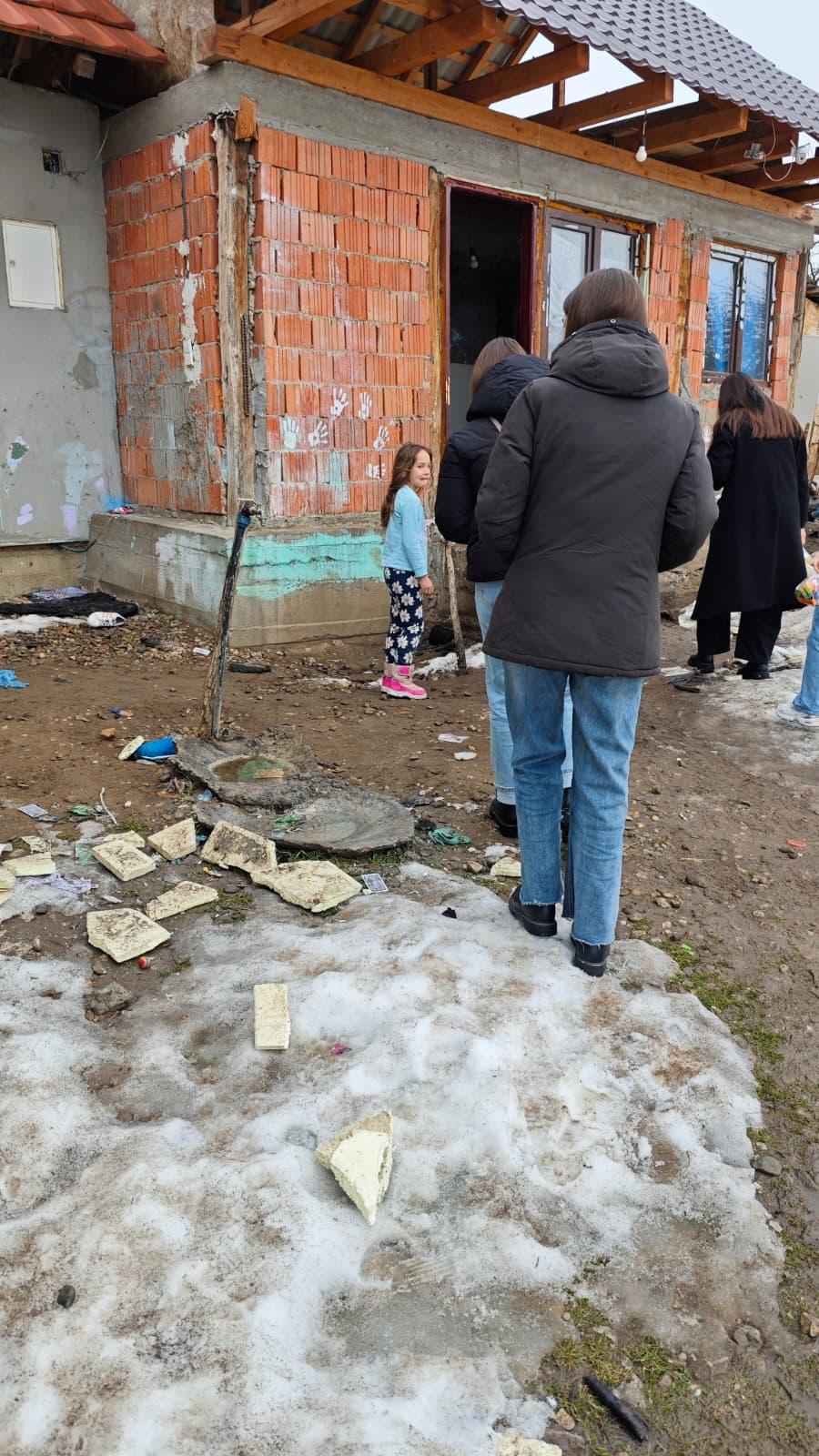 Fetița lângă casă de cărămidă cu voluntari