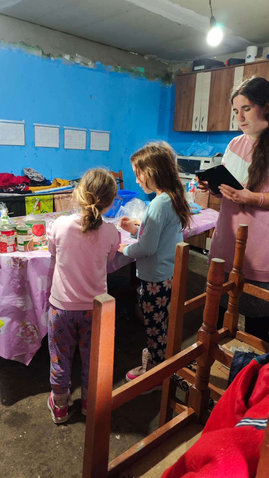 Două fetițe și o voluntară la masă cu conserve