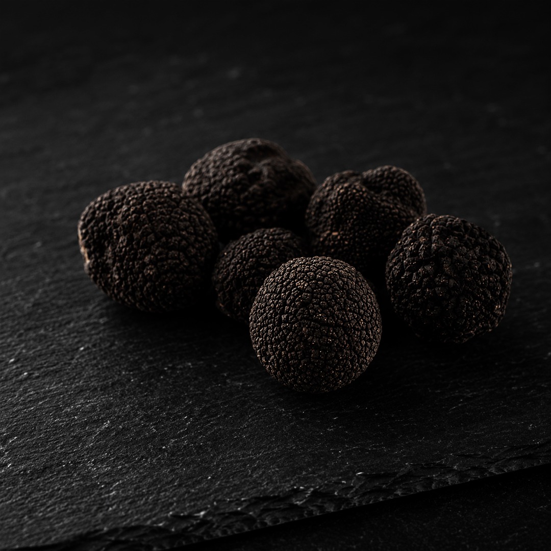 Six black truffles arranged on dark slate