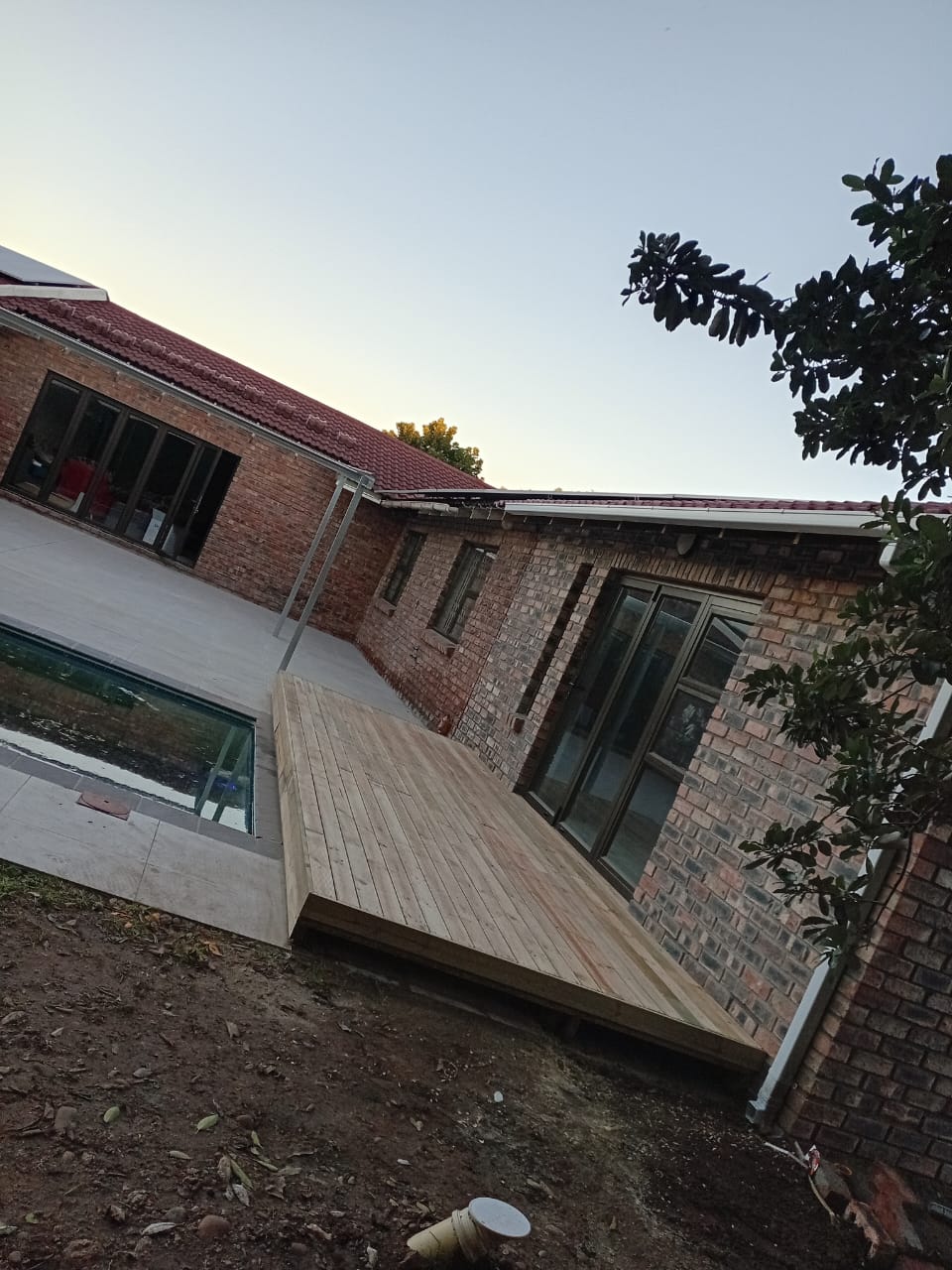 Finished wooden deck at dusk extending from brick house towards pool area, clean natural timber finish