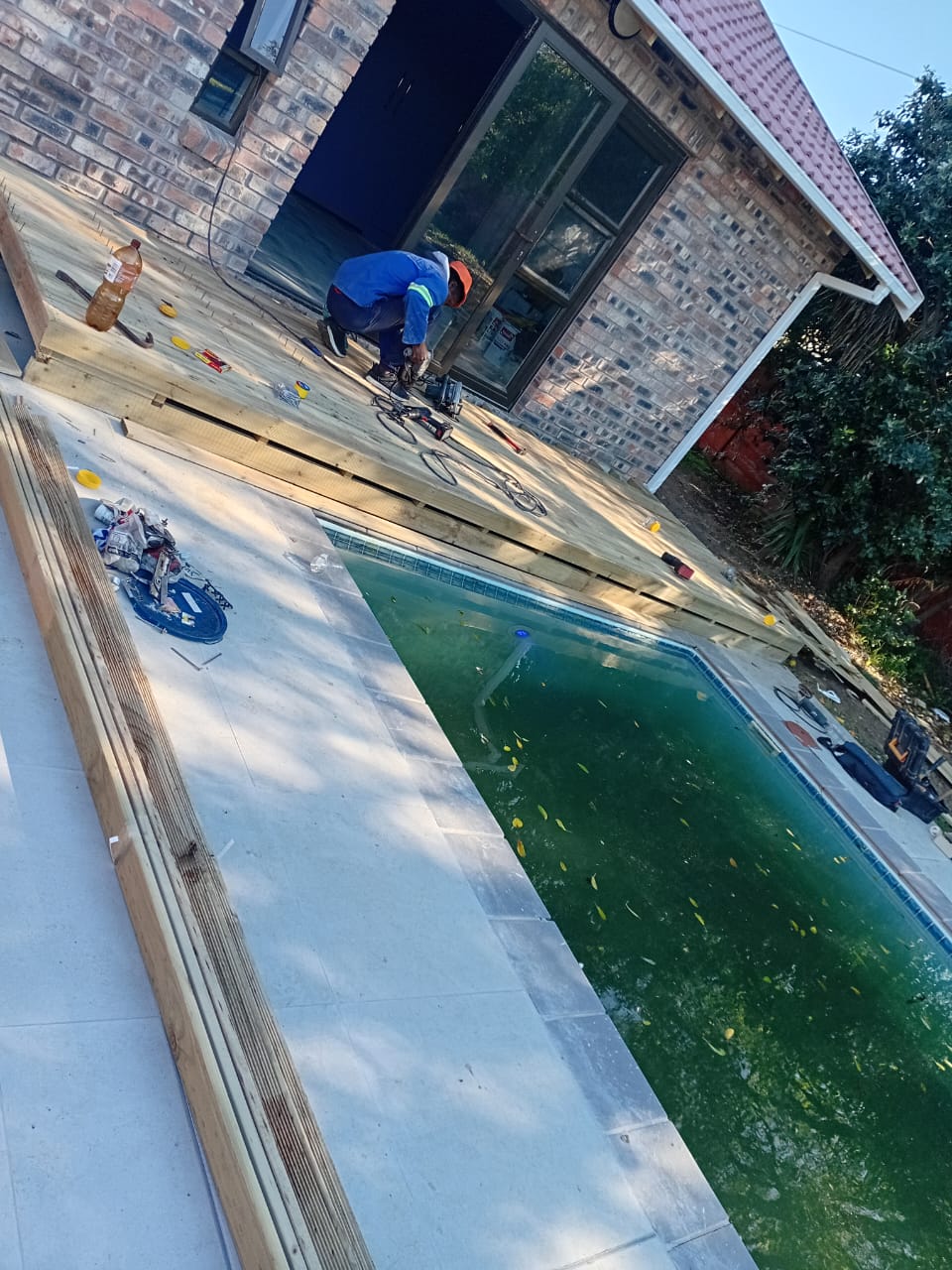 Angled view of worker securing deck boards, pool water visible, tools and equipment on deck surface