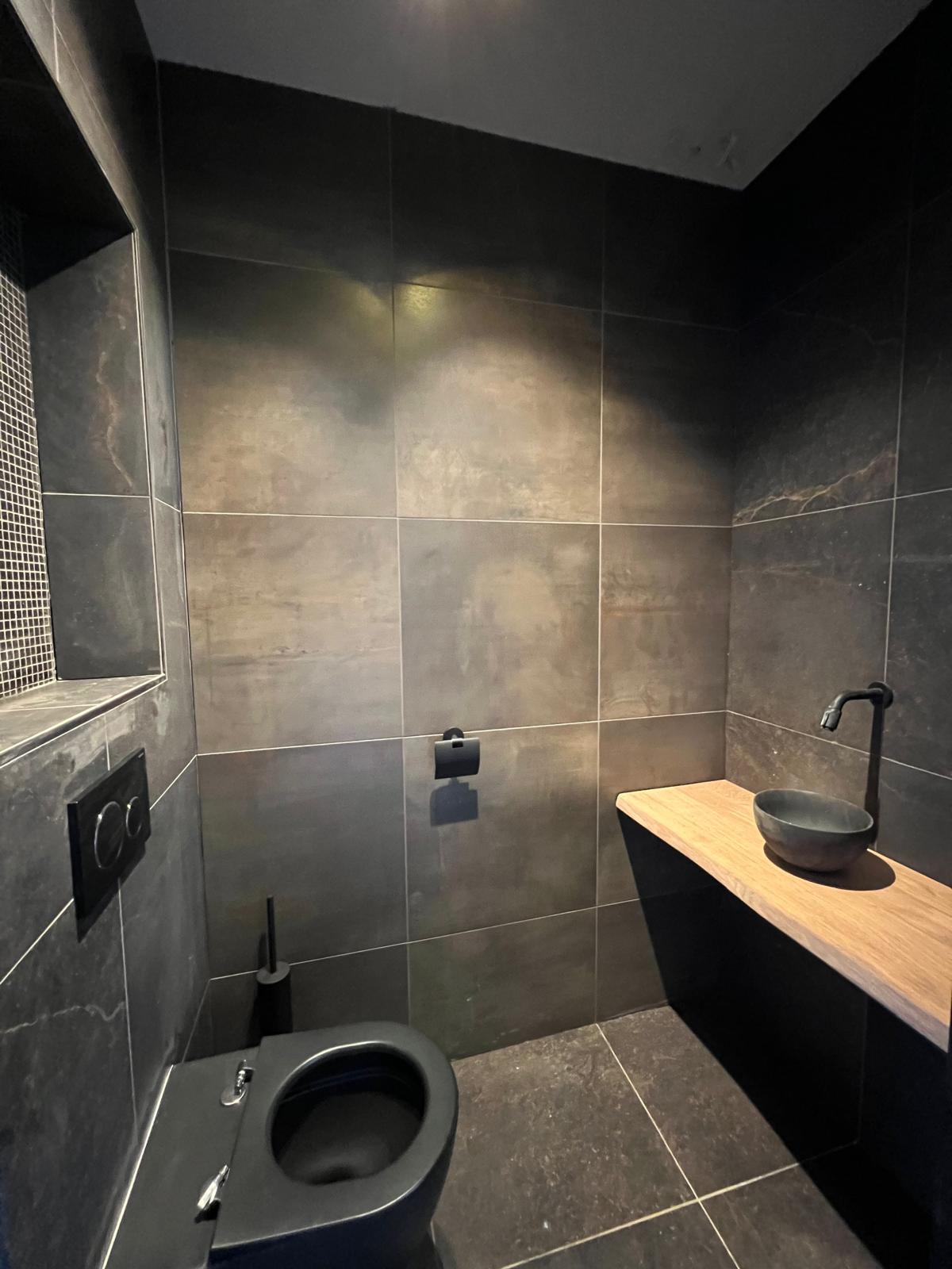 Toilet met donkere leisteen tegels en houten planchet