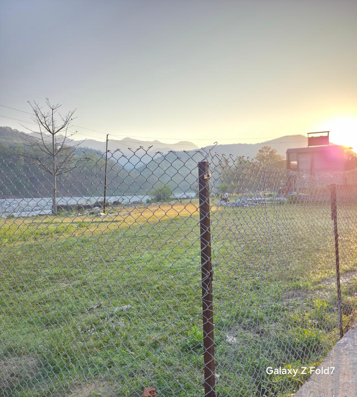 Open green fields at sunrise near Heaven River Retreat with Himalayan foothills in the background, Uttarakhand