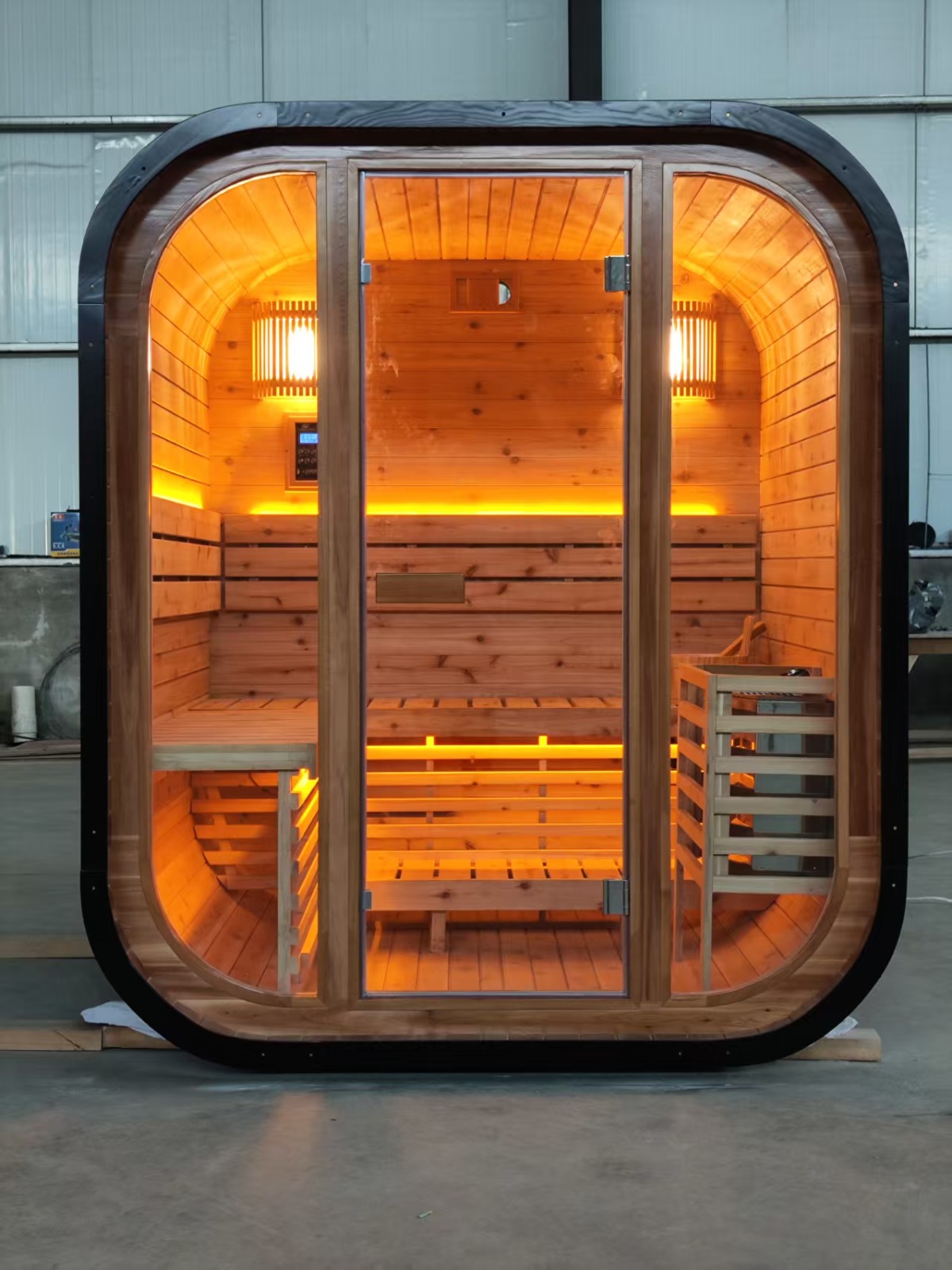 Front elevation of the finished cedar sauna with the glazed door closed and warm interior glow