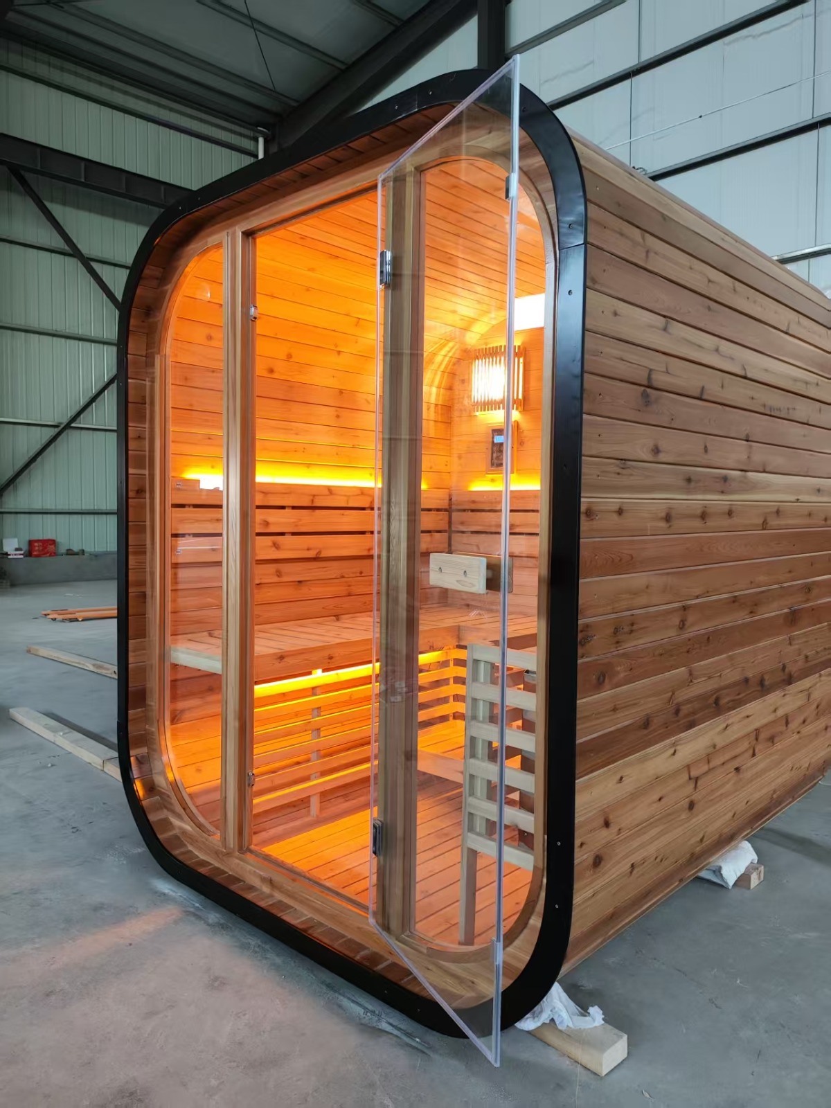 Angled view of the finished cedar sauna with the glass door open, showing the warm cedar interior and full-height glazing