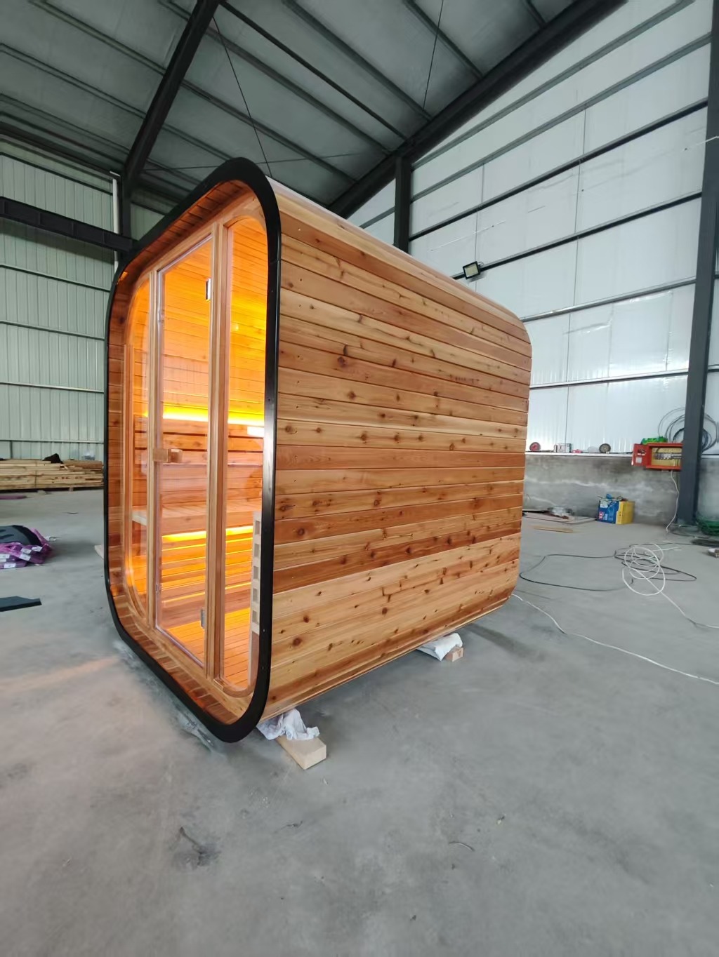 Three-quarter side view of the finished cedar sauna showing the horizontal cedar cladding and rounded profile