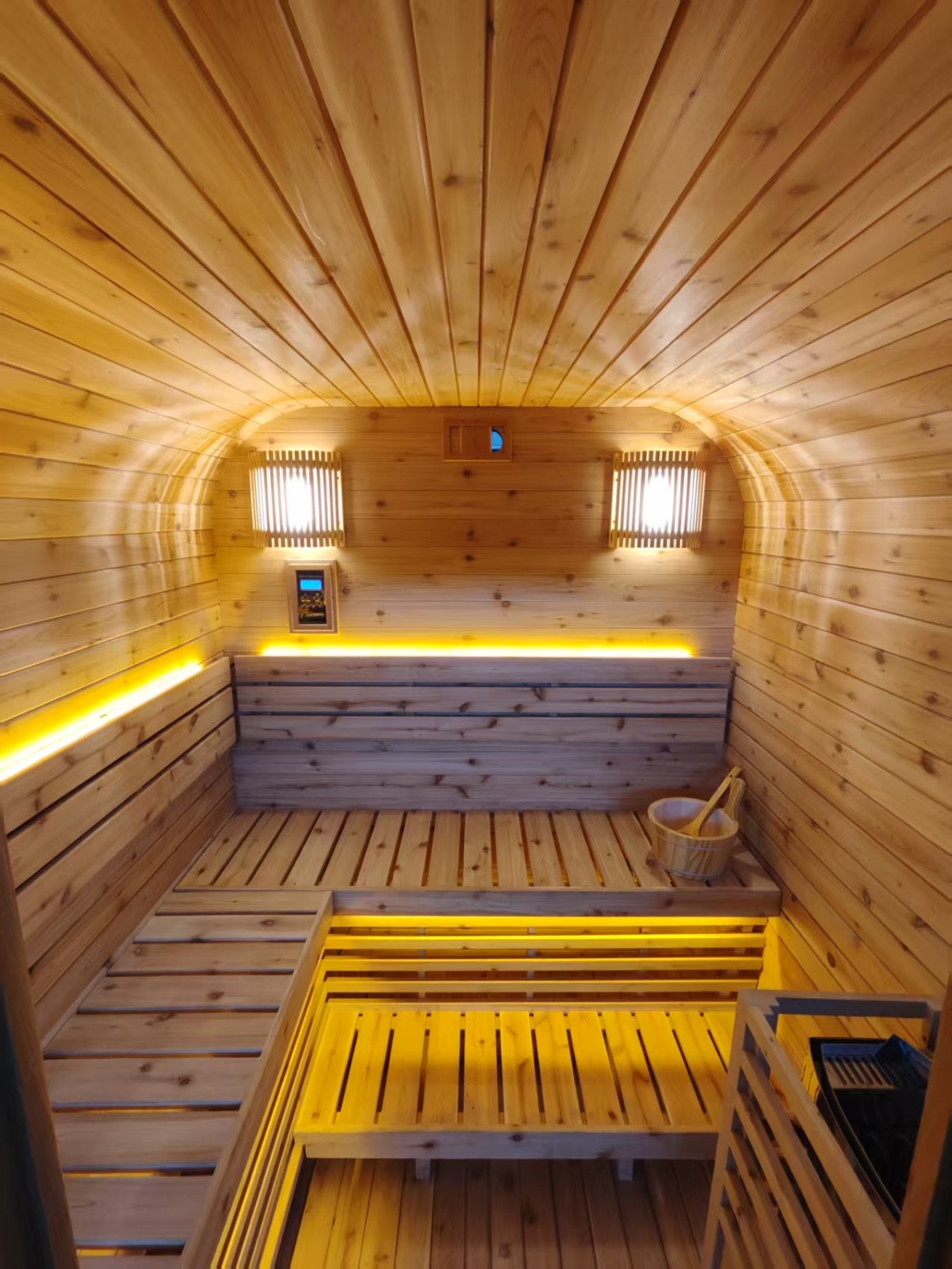 Wide interior view of the finished sauna showing the vaulted cedar ceiling, wall lights, digital control panel and two-tier bench seating