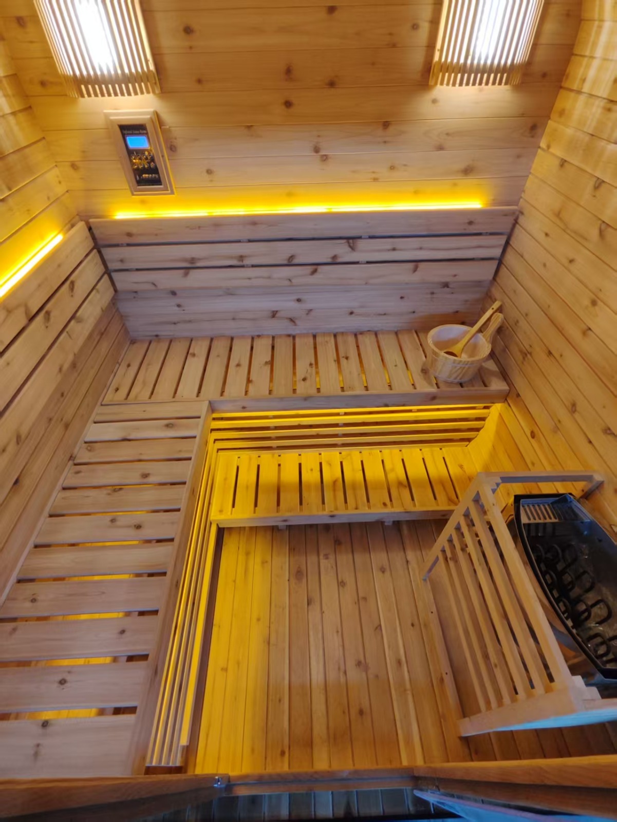Overhead view of the finished cedar interior showing two-tier bench seating, concealed LED lighting, digital controls and the Harvia electric heater