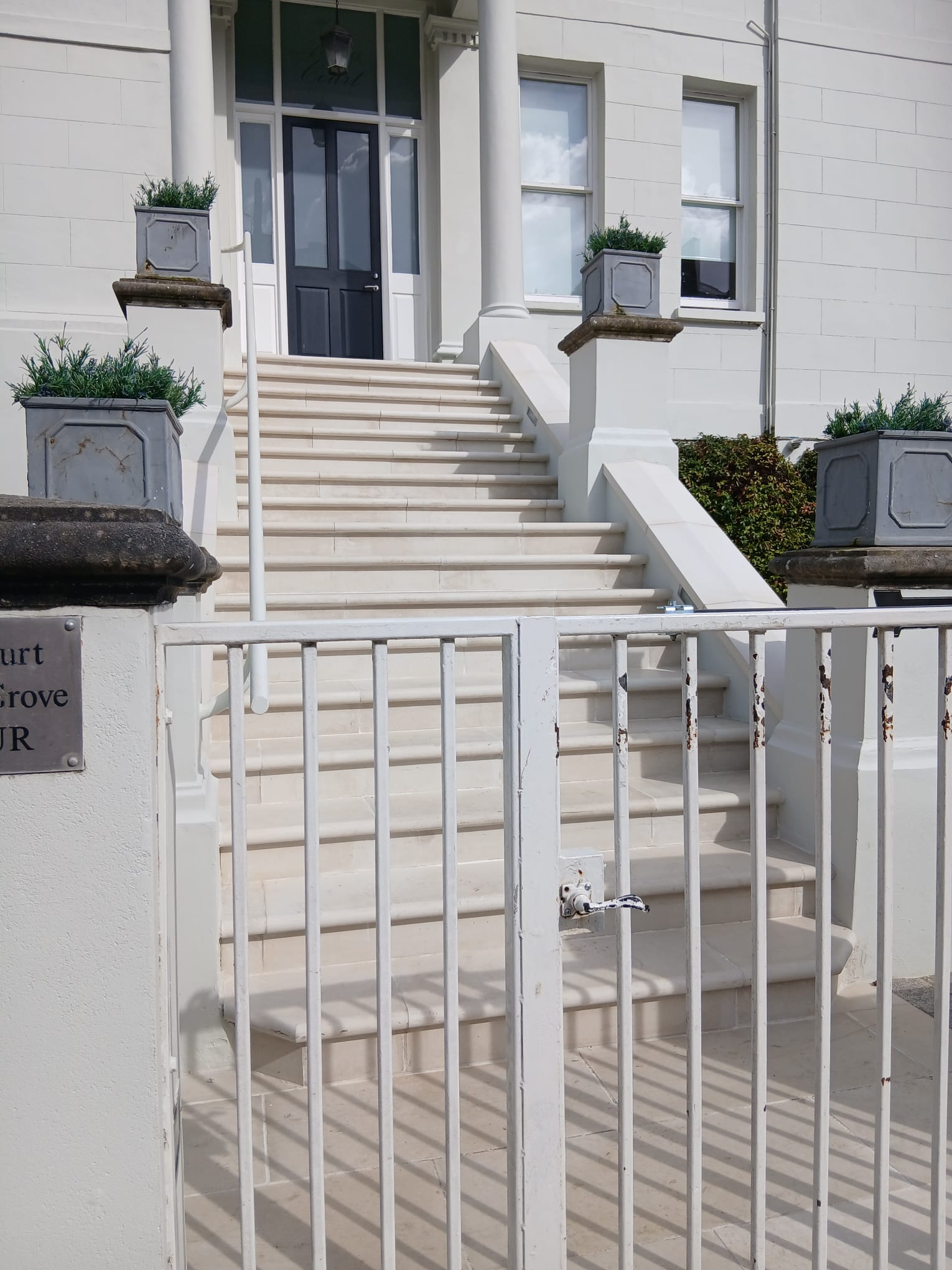 Grand entrance with restored pale stone front steps, stone pier planters and painted iron railings to a period building
