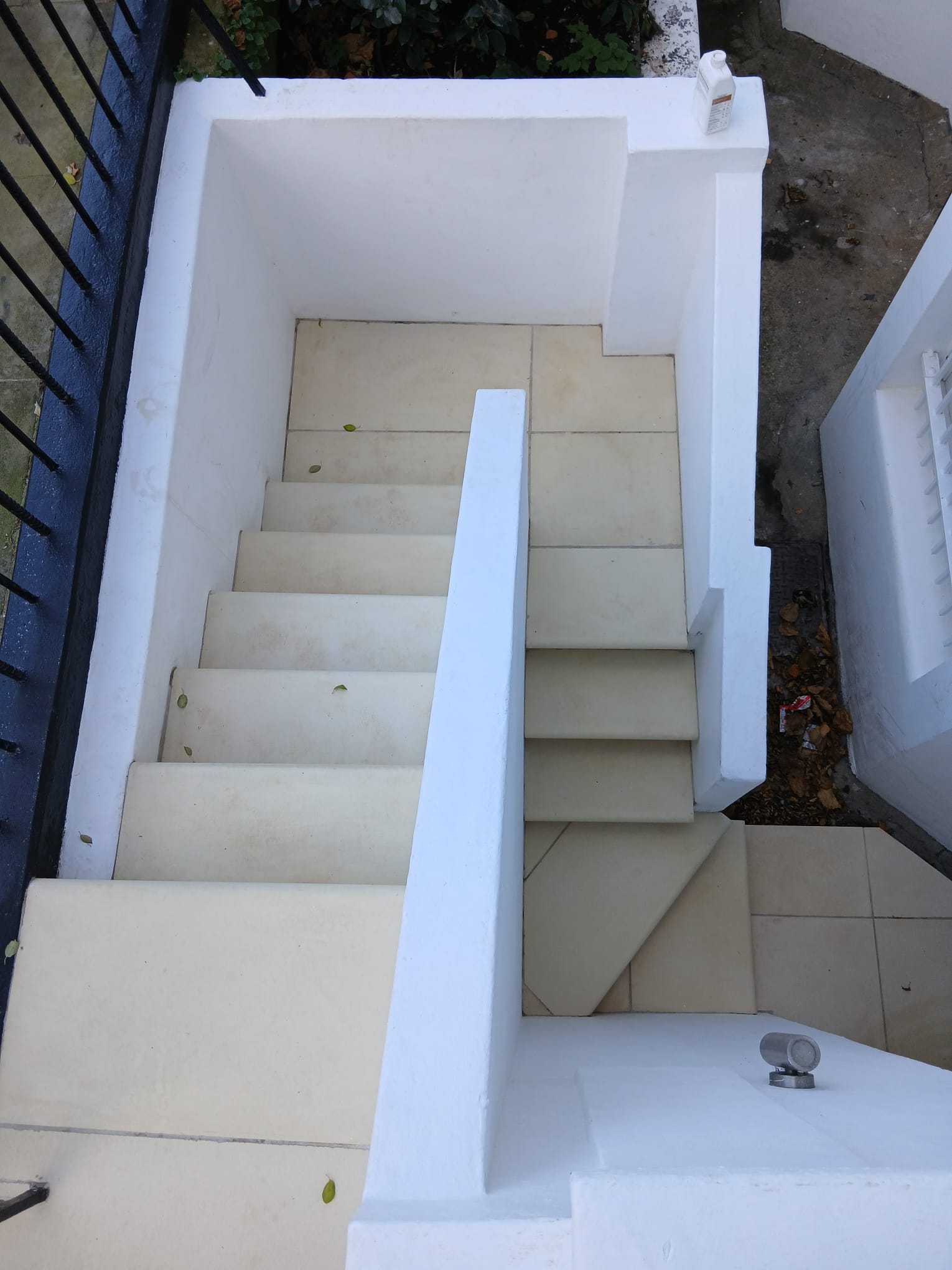 Exterior lightwell staircase with pale sandstone steps and freshly painted white rendered walls