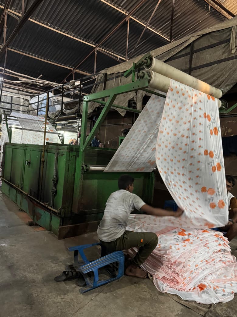 Worker at industrial rotary printing machine with printed fabric being produced