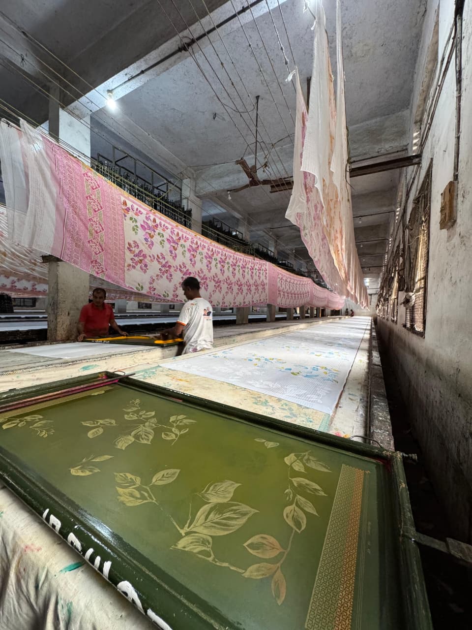 Screen printing with leaf design — worker at printing table with sarees hanging to dry in background