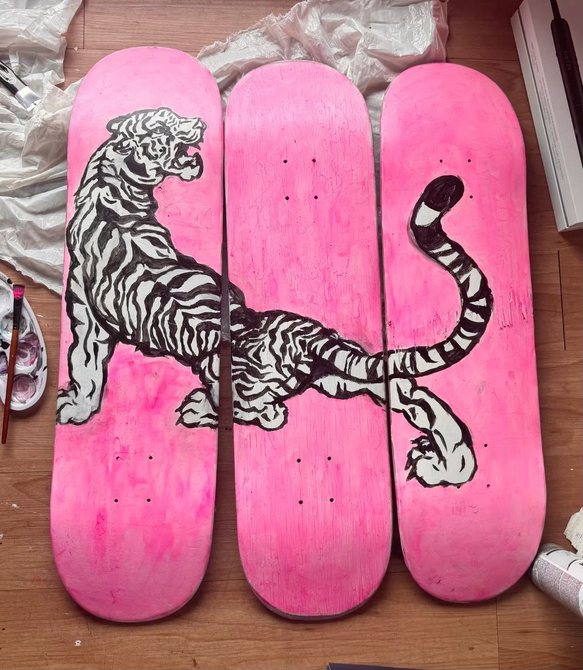 Bold black and white roaring tiger painted across three pink skateboard decks arranged as a triptych