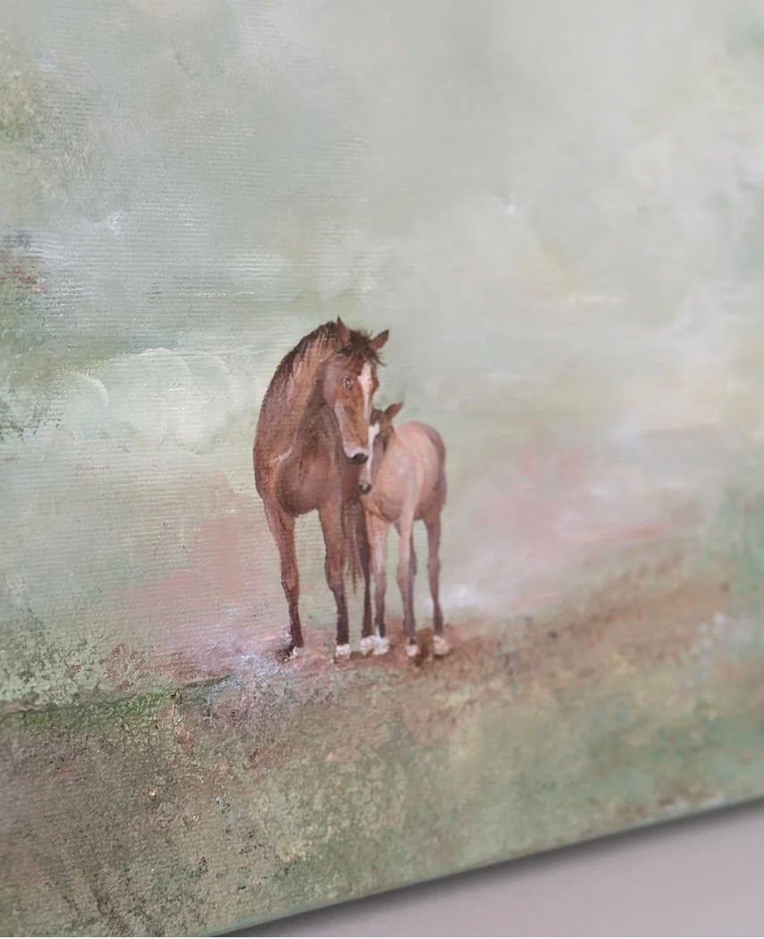 A brown mare and foal standing close together in a soft sage-green misty atmospheric field