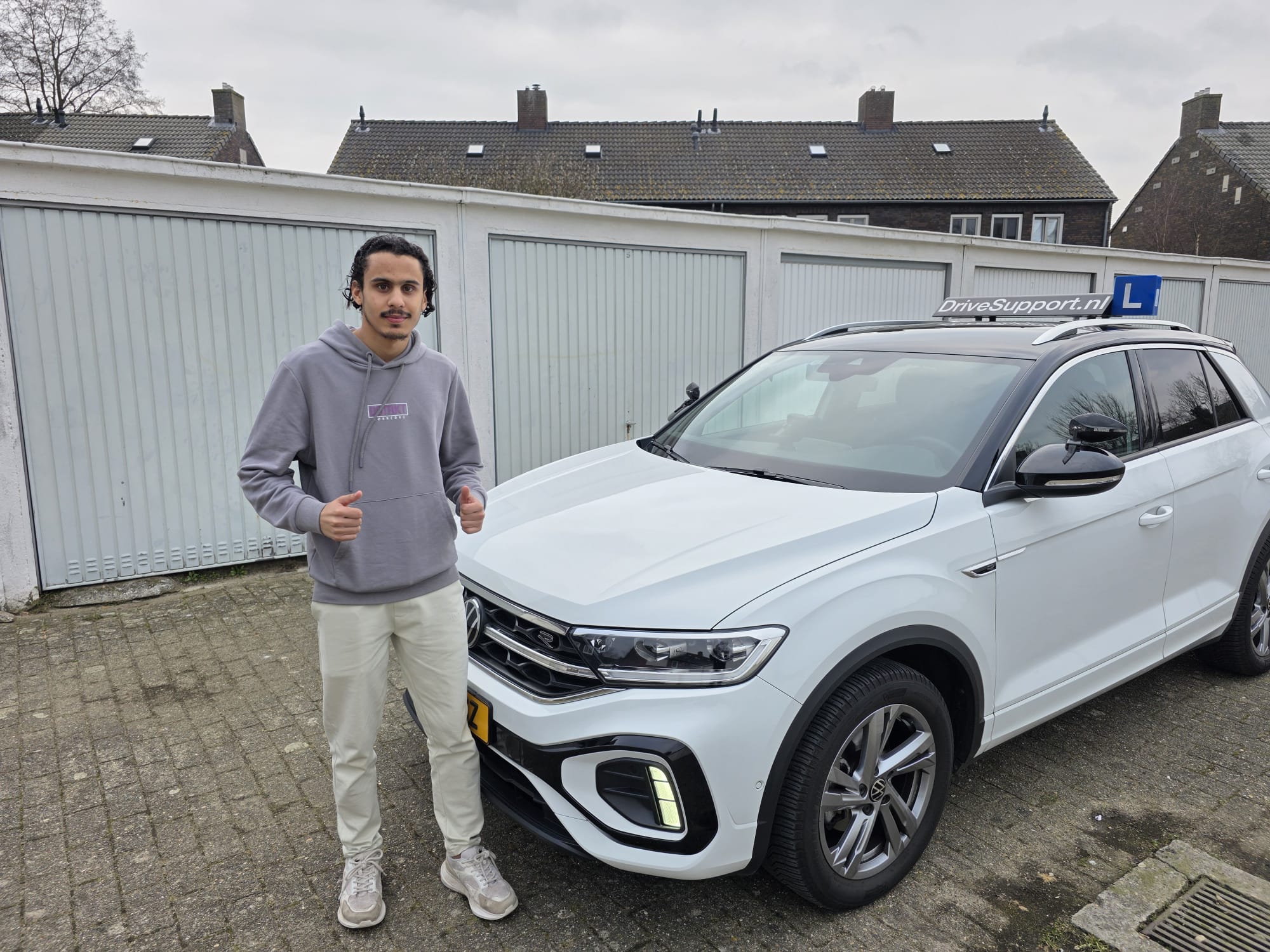 Leerling rijles Tilburg — duim omhoog naast de DriveSupport lesauto in een Tilburgse straat