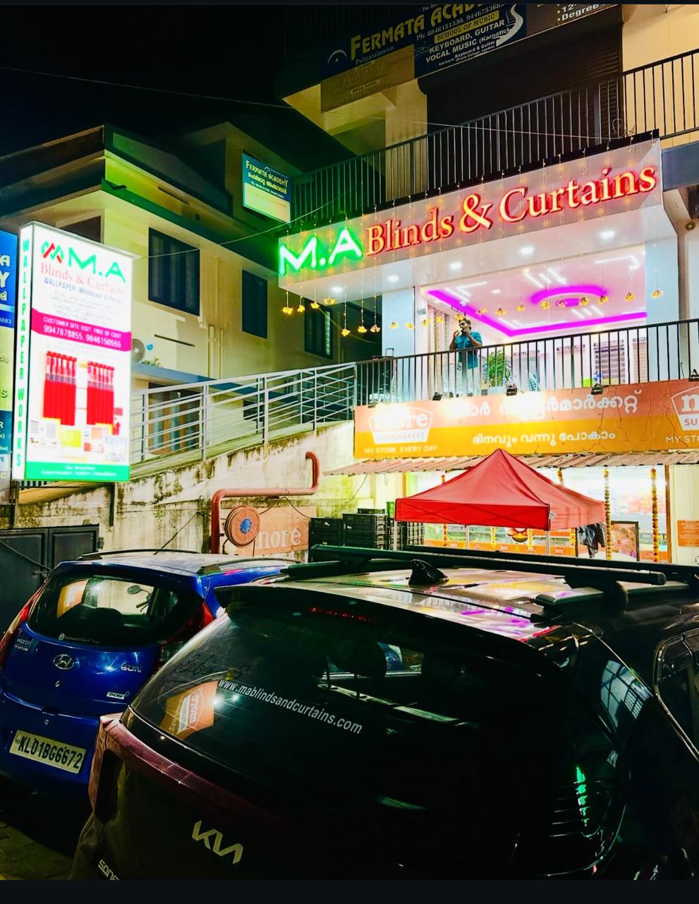 M.A Blinds & Curtains storefront glowing with neon sign and string lights at night by M.A Blinds & Curtains
