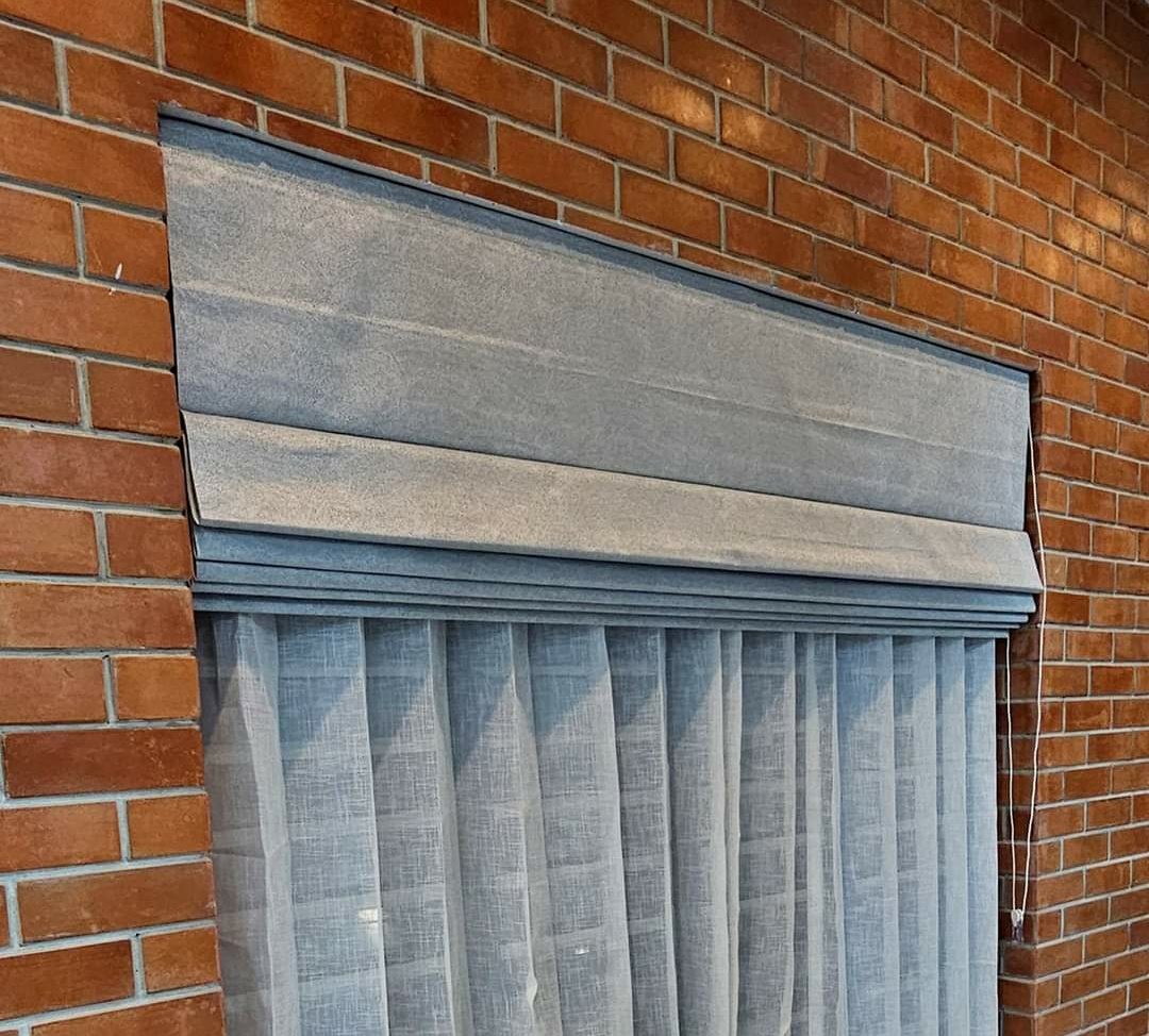 Grey pelmet valance over sheer curtains mounted on a brick wall by M.A Blinds & Curtains