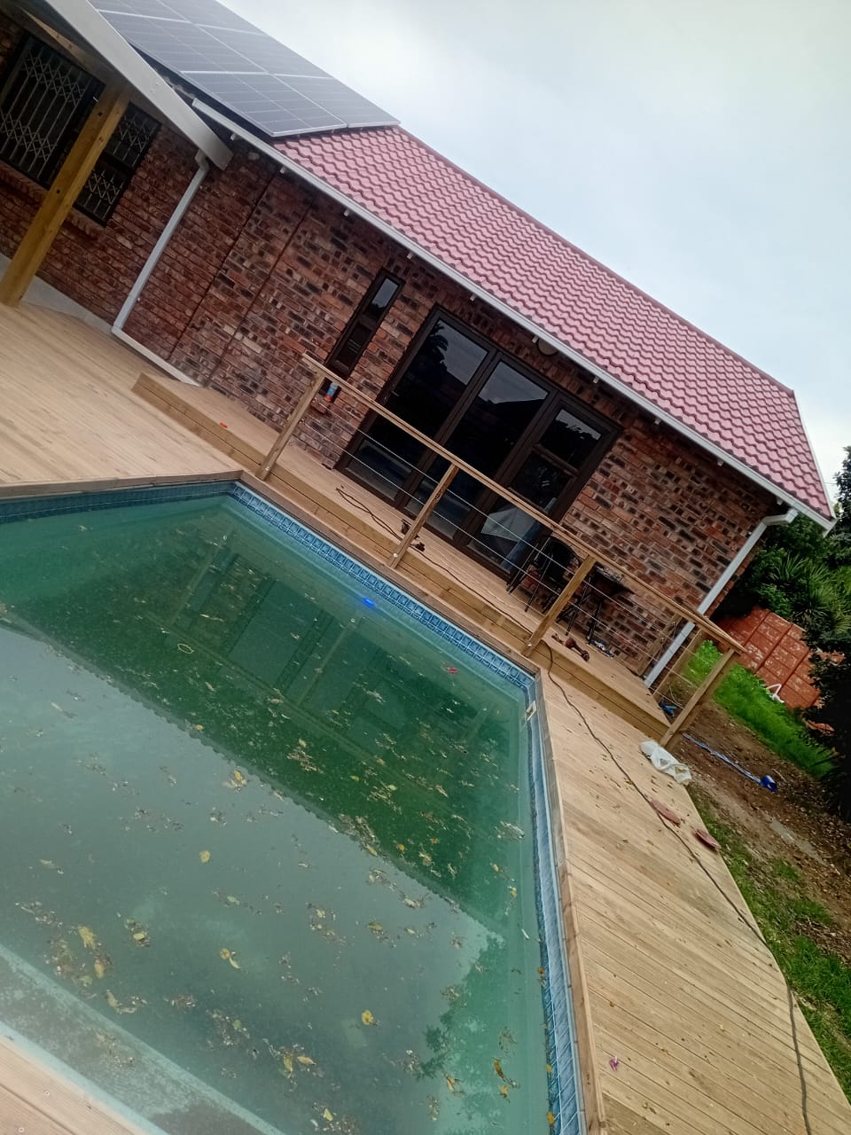 Completed swimming pool wooden deck Port Elizabeth — full wrap-around natural pine deck with stainless steel balustrade and solar panel brick house