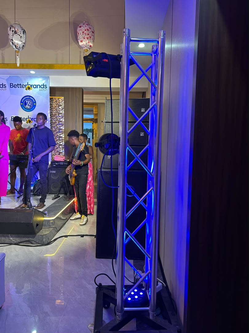 Indoor live band performance with blue LED-lit metal truss, guitar player, DJ equipment, Betterbrands event