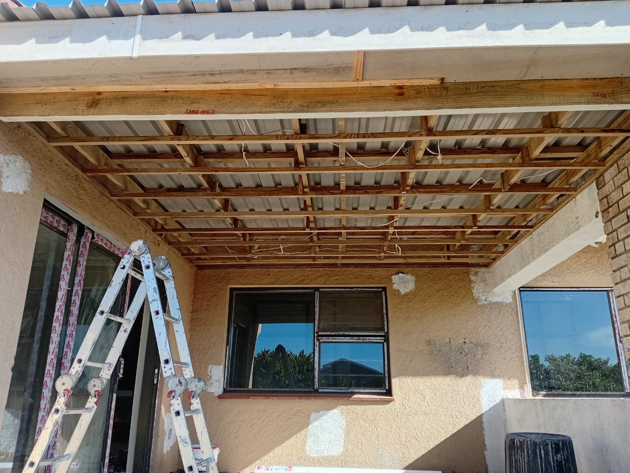 Flat roof interior framing Port Elizabeth — wooden beam structure with metal sheeting, electrical conduits, and internal view of asbestos removal