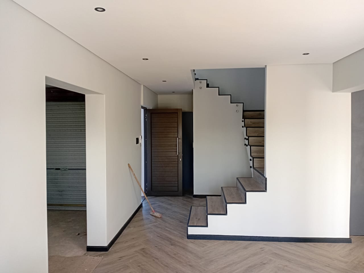 Interior painting Port Elizabeth — entrance hall with white walls, recessed lighting, floating staircase with glass balustrade, herringbone vinyl floor