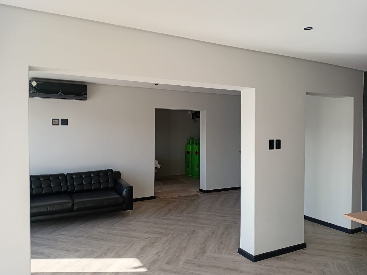 Interior painting Gqeberha — lounge with light grey walls, white recessed ceiling, open archway, herringbone vinyl flooring and black leather sofa