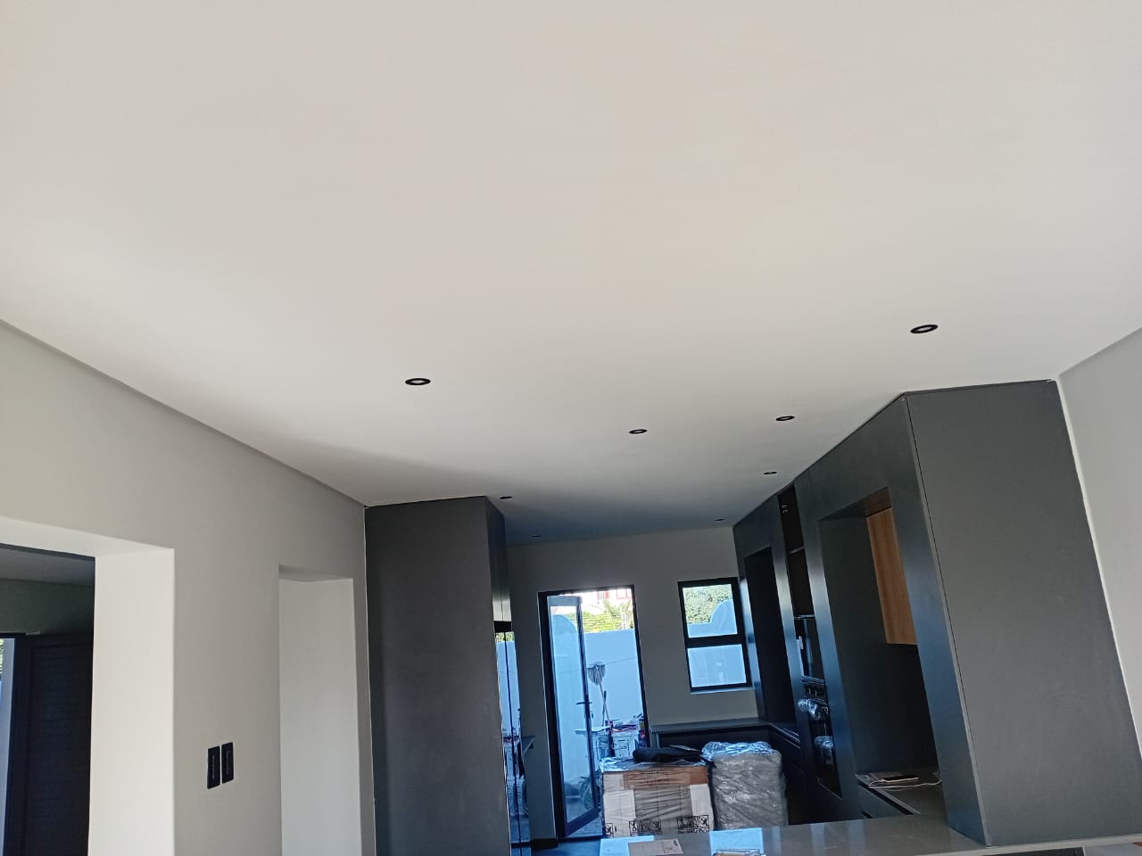 Interior painting Gqeberha — white walls with recessed downlights, charcoal grey cabinetry, folding door and window with garden view