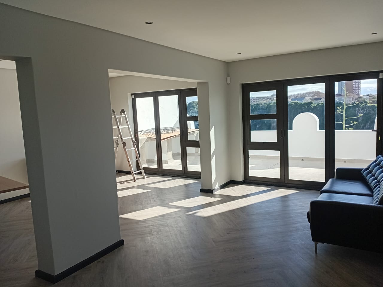 Interior painting Port Elizabeth — bright open plan with white painted walls and columns, large folding doors, herringbone floor, sofa visible