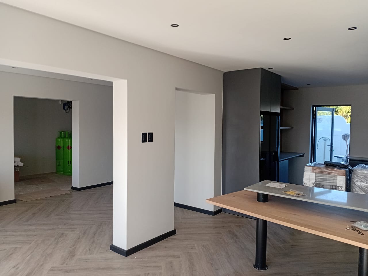 Interior painting Port Elizabeth — open plan with white walls and grey feature wall, charcoal cabinetry, island bench, recessed downlights, herringbone floor