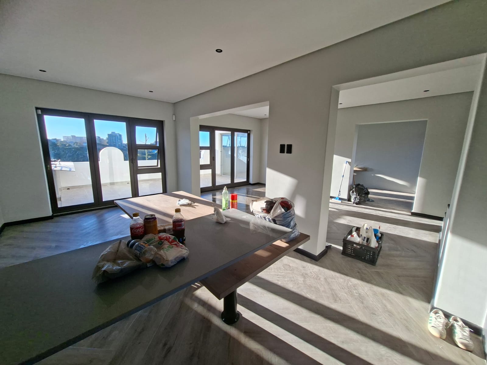 Interior painting Port Elizabeth — wide open plan with light grey walls, two sets of dark-framed doors, island bench and kitchen, workers finishing up