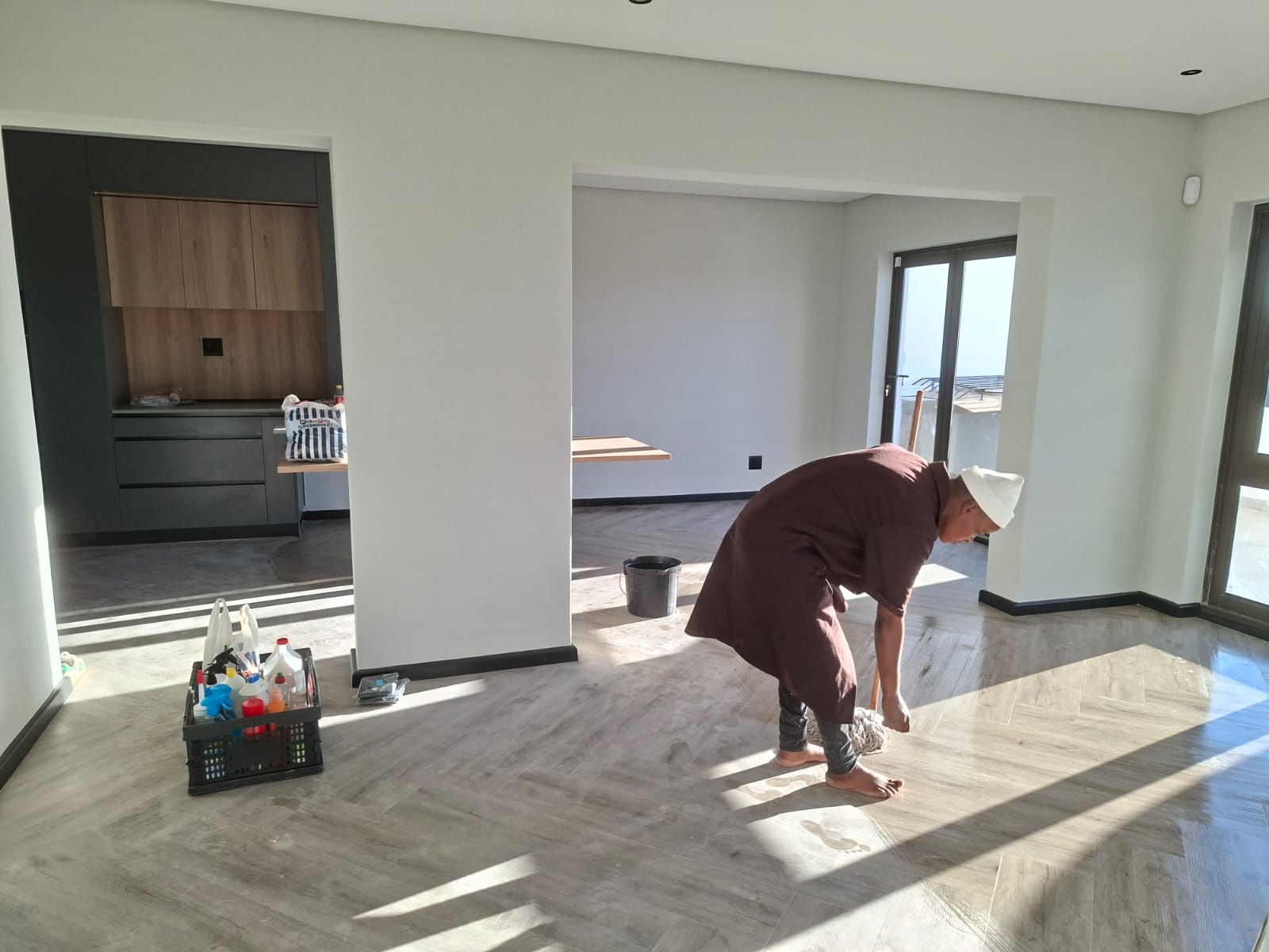 Interior painting Port Elizabeth — open plan with white walls, charcoal TV wall feature, herringbone floor, worker doing final clean at handover