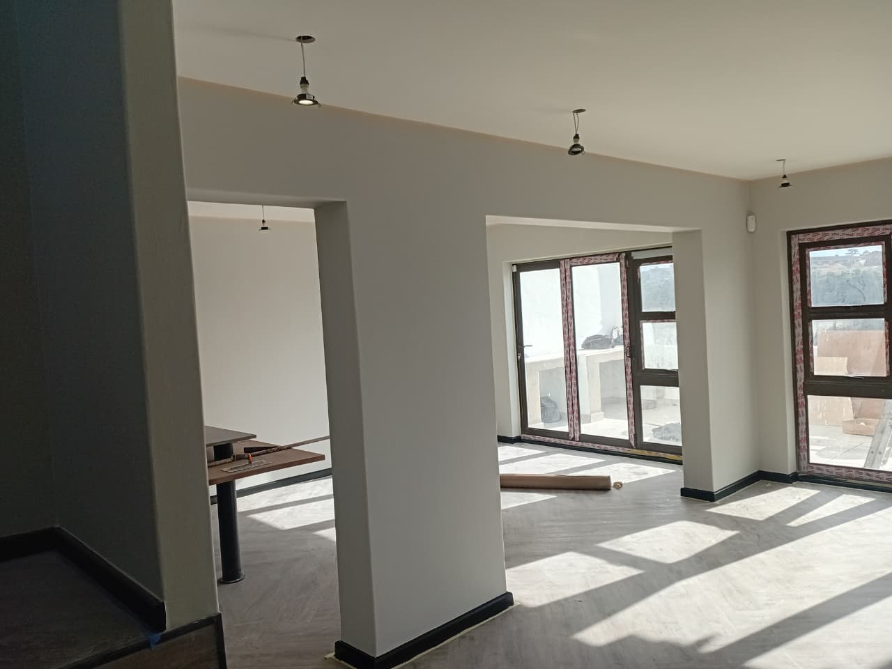 Interior painting Port Elizabeth — bright open plan living area with white plastered walls, recessed downlights, large folding doors opening to balcony