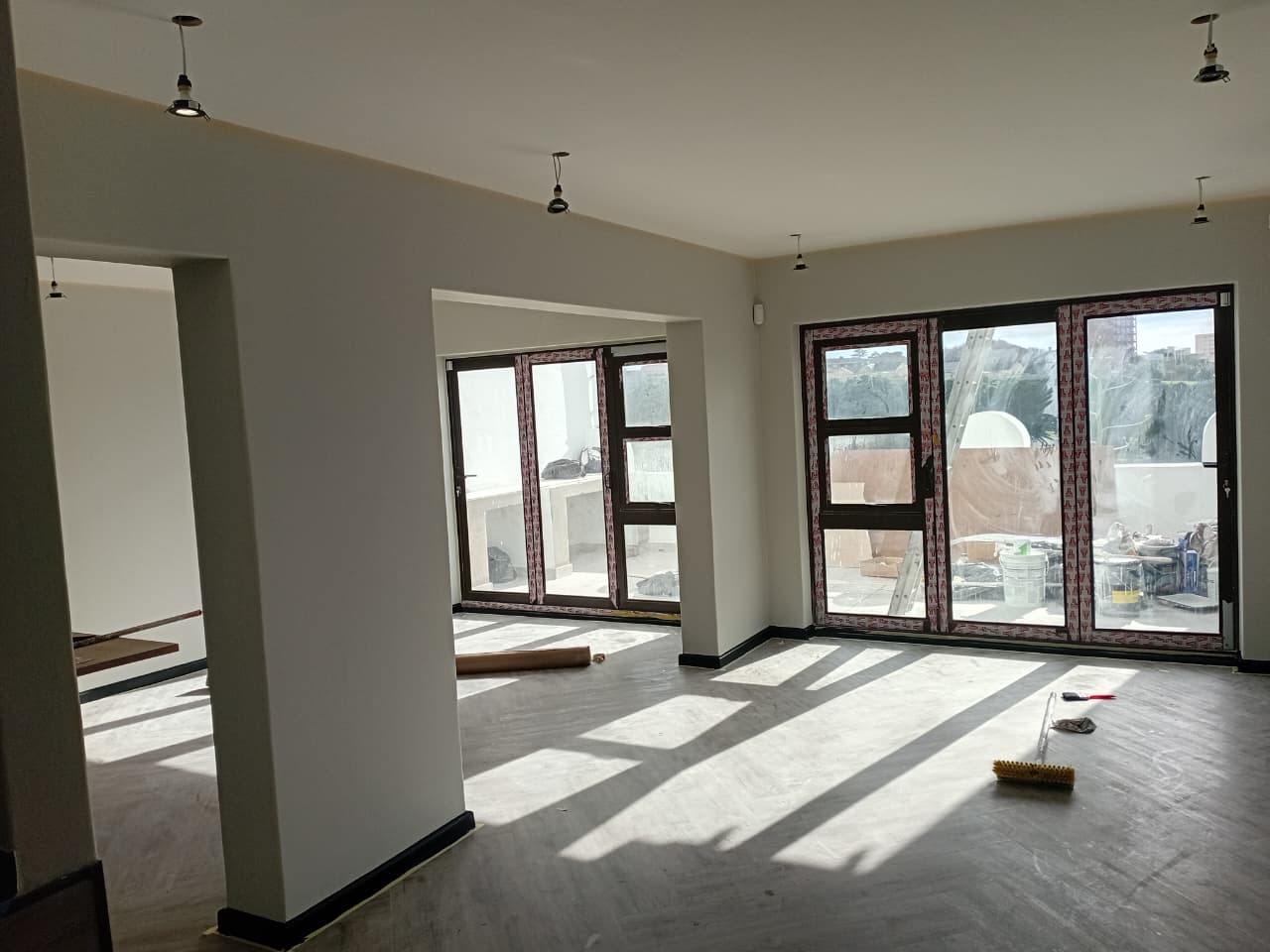 Interior painting Port Elizabeth — large open plan room with freshly painted white walls, two sets of dark-framed folding doors, floor paint protection still down