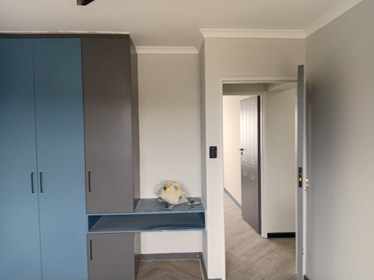 Interior painting Port Elizabeth — bedroom with blue and grey painted wardrobes, grey cornice, doorway leading to corridor with white panelled doors
