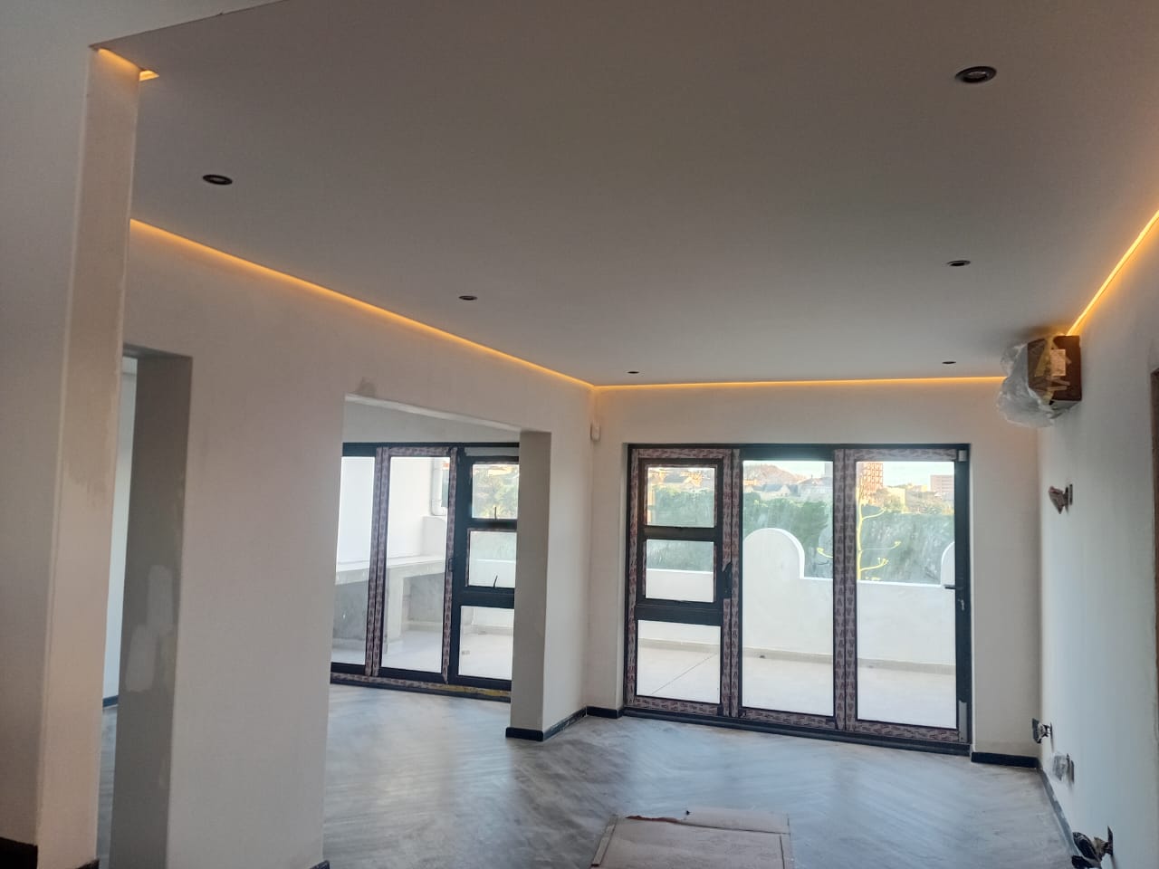 Interior painting Gqeberha — white plastered walls with recessed downlights and amber LED strip cove, large folding doors, balcony city view