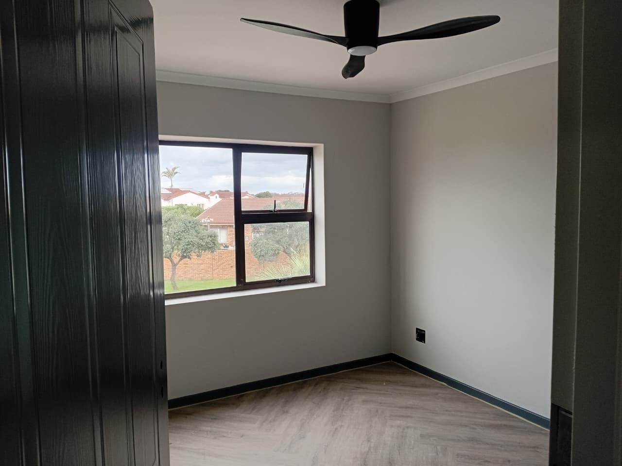 Interior painting Port Elizabeth — bedroom with light warm grey walls, white cornice, black ceiling fan, dark aluminium window framing garden view