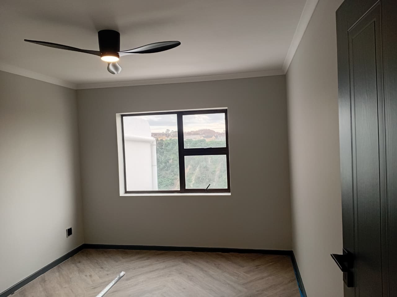 Interior painting Port Elizabeth — bedroom with warm grey walls, white cornice, black ceiling fan, herringbone vinyl floor and garden view window