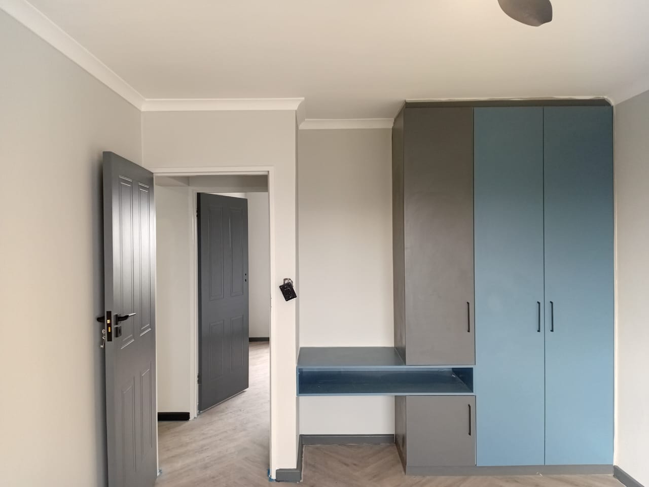 Interior painting Port Elizabeth — bedroom with light grey walls, white cornice, built-in blue and grey wardrobes, herringbone floor