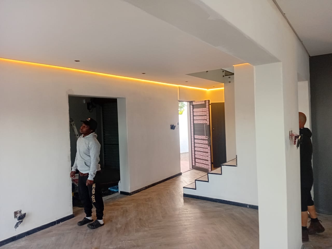 Interior painting Gqeberha — open plan lounge with amber LED strip cove, white walls, floating staircase, Osflex Construction worker inspecting finish
