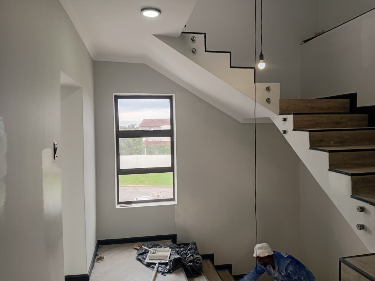 Interior painting Port Elizabeth — stairwell with grey painted walls, glass and steel floating staircase, pendant light and garden-view window