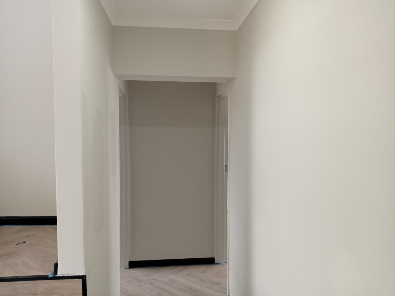 Interior painting Gqeberha — narrow white-painted hallway with ornate white cornice, herringbone vinyl floor, leading to open doorway